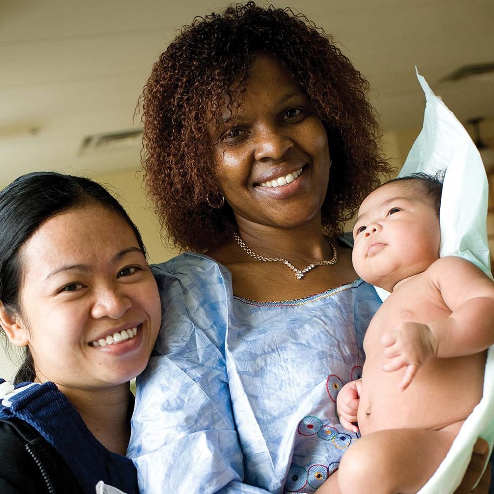 Association of Ontario Midwives. Smiling midwife holding client's baby.