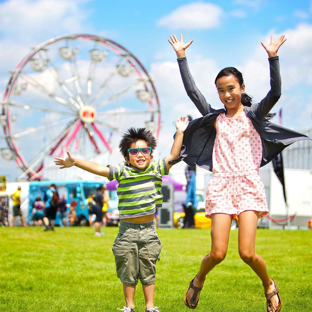 2016 Discovery Guide Cover. Young boy and girl jumping in the air at an outdoor festival.
